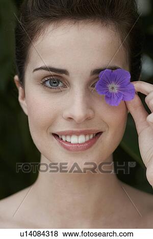 Stock Photo - Young woman holding flower over her eye. Fotosearch
