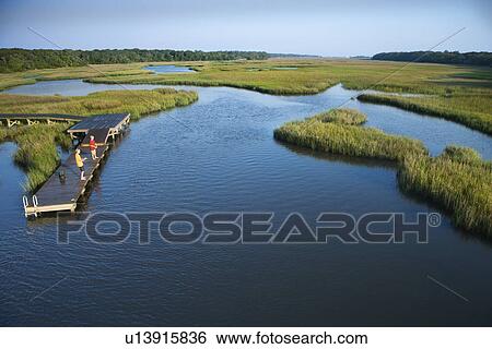 Stock Photograph - Aerial view of two teenage boys fishing from dock in marshy lowlands of Bald Head Island, North Carolina. Fotosearch