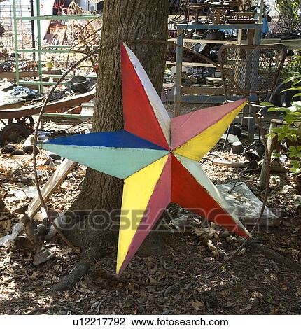 Stock Image - Colorful painted star made of metal leaning against tree.. Fotosearch