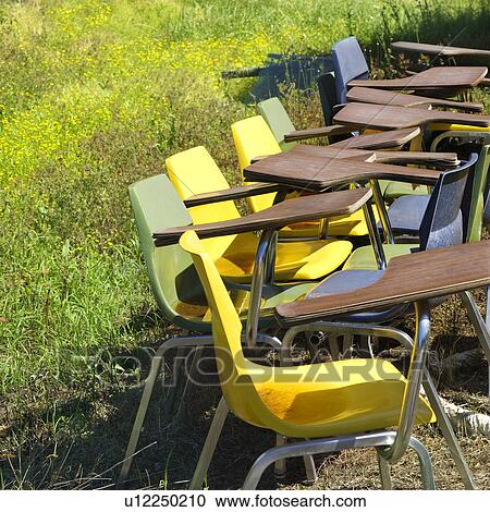 Stock Image - Old school chairs in grassy field.. Fotosearch