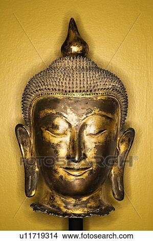 Picture - Bronze Buddha head from Thailand against yellow wall. Fotosearch