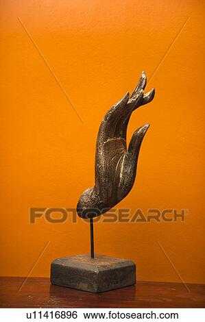 Stock Photograph - Carved hand sculpture from Thailand against orange wall.. Fotosearch