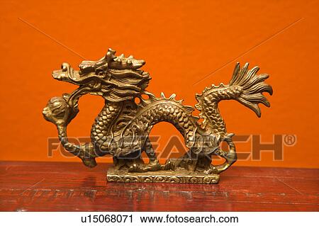 Stock Image - Chinese Taoist wisdom brass dragon statue against orange wall.. Fotosearch