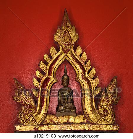 Stock Image - Golden Buddha statue against red wall.. Fotosearch