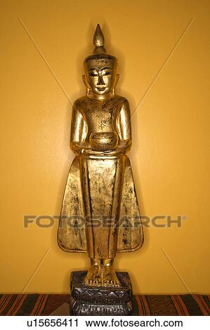 Stock Image - Golden wooden Buddha statue from Myanmar against yellow wall.. Fotosearch