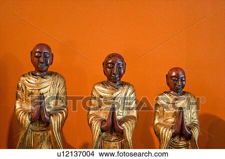 Three wooden statues of Buddhist disciples against orange wall. View Large Photo Image Picture - Three wooden statues of Buddhist disciples against orange wall.. Fotosearch