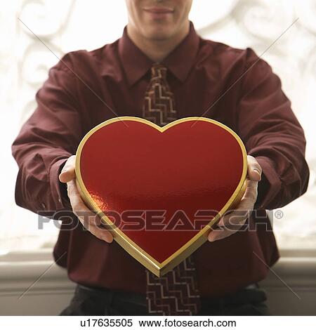 Stock Photography - Man holding a heart shaped box of chocolates. Fotosearch