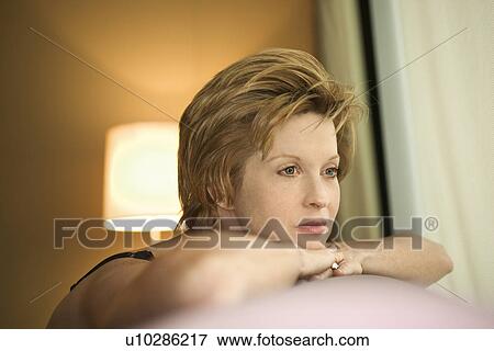 Stock Photo - Portrait of pretty woman draped over sofa by window looking out.. Fotosearch