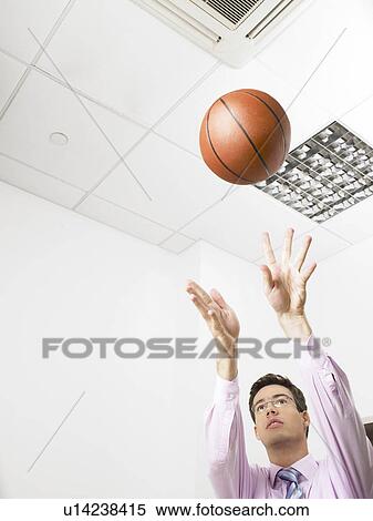 Stock Photography - Businessman in an office throwing a basketball. Fotosearch