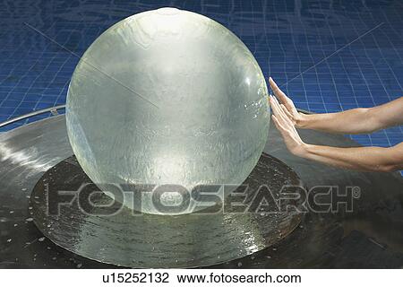 Stock Image - Hands almost touching water globe.. Fotosearch