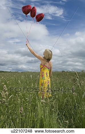 Stock Photo - Woman holding balloons in field. Fotosearch