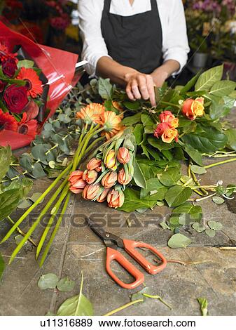 Stock Photo - Young female florist preparing bouquet in shop, mid section. Fotosearch
