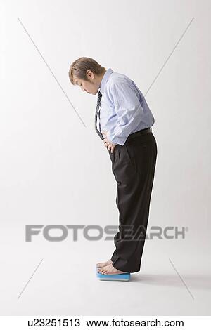 Stock Image - Businessman standing on bathroom scale. Fotosearch
