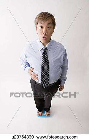Stock Image - Businessman standing on bathroom scale. Fotosearch