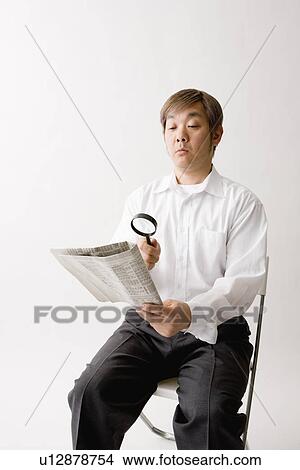 Picture - Mature man reading newspaper with magnifying glass. Fotosearch