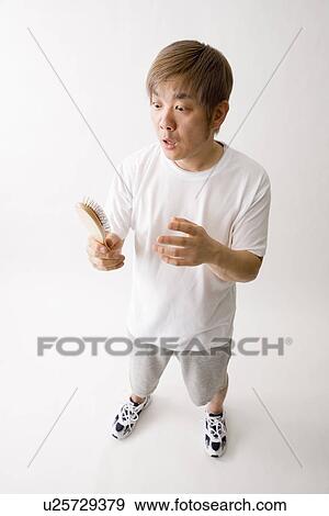 Stock Photo - Mid adult man looking at hair brush. Fotosearch