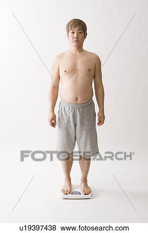 Stock Photo - Mid adult man standing on bathroom scale. Fotosearch