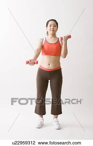 Stock Image - Mid adult woman exercising with dumbbells. Fotosearch