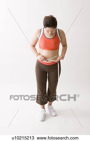 Stock Image - Mid adult woman measuring her waist. Fotosearch