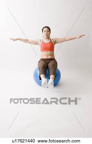 Stock Image - Mid adult woman sitting on fitness ball. Fotosearch
