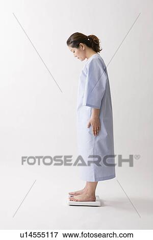Stock Photo - Mid adult woman standing on bathroom scale. Fotosearch