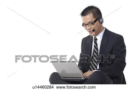 Businessman working on a laptop and wearing a headset View Large Photo Image Picture - Businessman working on a laptop and wearing a headset. Fotosearch