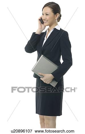 Stock Photo - Businesswoman holding a laptop and talking on a mobile phone. Fotosearch