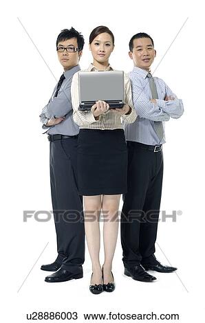 Stock Image - Businesswoman holding a laptop with two businessmen standing behind her. Fotosearch
