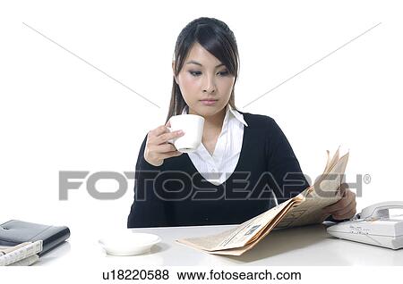 Stock Photo - Businesswoman reading a financial newspaper and holding a tea cup. Fotosearch