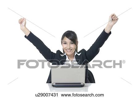 Stock Image - Businesswoman working on a laptop and raising her hands. Fotosearch