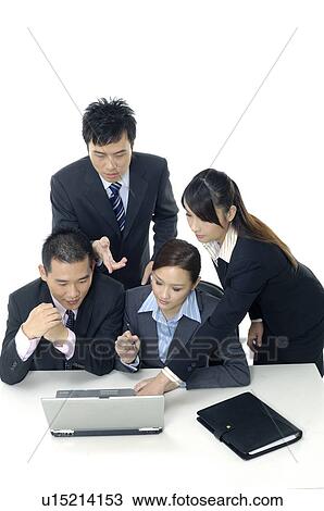 Stock Image - Two businessmen and two businesswomen working on a laptop. Fotosearch
