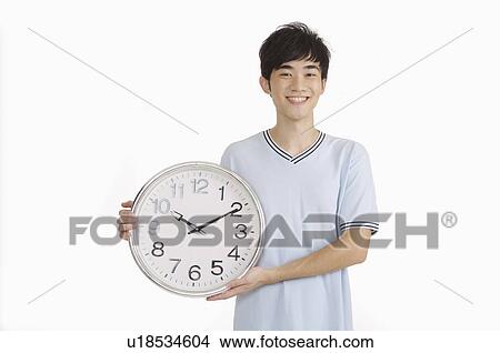 Young man holding a clock and smiling at the camera View Large Photo Image Picture - Young man holding a clock and smiling at the camera. Fotosearch