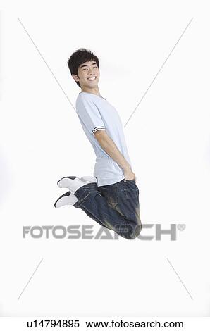 Stock Photography - Young man jumping in mid-air with hands in pockets and smiling. Fotosearch