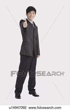 Stock Image - Young man standing with thumbs up and smiling. Fotosearch