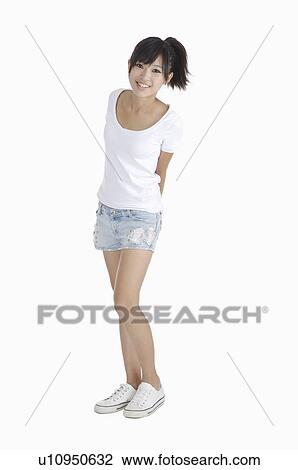 Young woman standing with hands behind back and smiling at the camera View Large Photo Image Stock Image - Young woman standing with hands behind back and smiling at the camera. Fotosearch