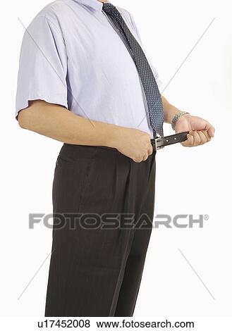 Stock Photo - Man standing and squeezing waist with belt for dieting. Fotosearch