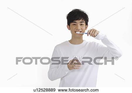 Stock Photo - Young man holding a cup and brushing teeth. Fotosearch
