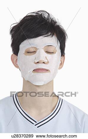 Stock Photo - Young man putting facial mask on face for skin care. Fotosearch