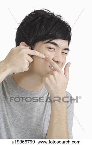 Stock Photo - Young man squeezing acne and winking. Fotosearch