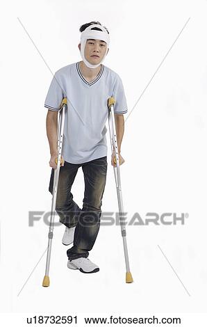 Stock Image - Young man standing with crutch and having adhesive bandage on head. Fotosearch