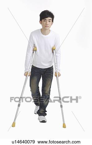 Stock Photo - Young man standing with crutch for sprain on leg. Fotosearch