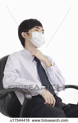 Stock Photograph - Young man touching throat and wearing surgical mask. Fotosearch
