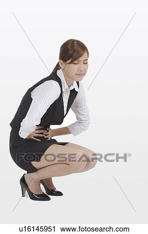Stock Image - Young office lady crouching and frowning of stomachache. Fotosearch