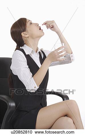 Young office lady holding a glass of water and taking medicine View Large Photo Image Stock Image - Young office lady holding a glass of water and taking medicine. Fotosearch