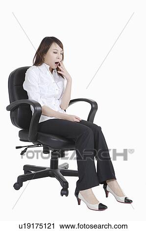 Stock Image - Young office lady sitting on chair and yawning of exhaustion. Fotosearch