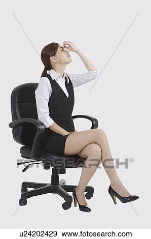 Stock Photo - Young office lady sitting on chair and closing eyes of exhaustion. Fotosearch