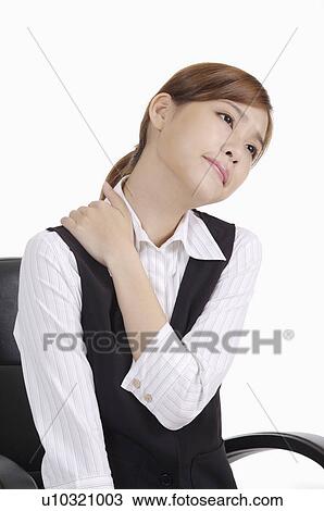 Stock Image - Young office worker sitting and putting hand on shoulder of exhaustion. Fotosearch