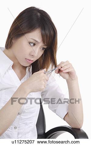 Young woman cutting hair with scissors and looking away View Large Photo Image Stock Photo - Young woman cutting hair with scissors and looking away. Fotosearch