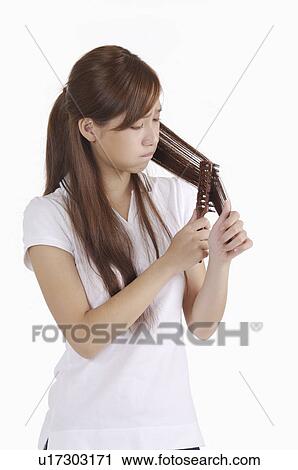 Stock Image - Young woman holding comb on hair and looking away. Fotosearch