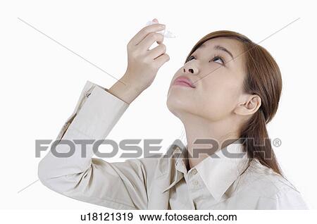Stock Photo - Young woman holding eyedropper and applying to her eyes. Fotosearch